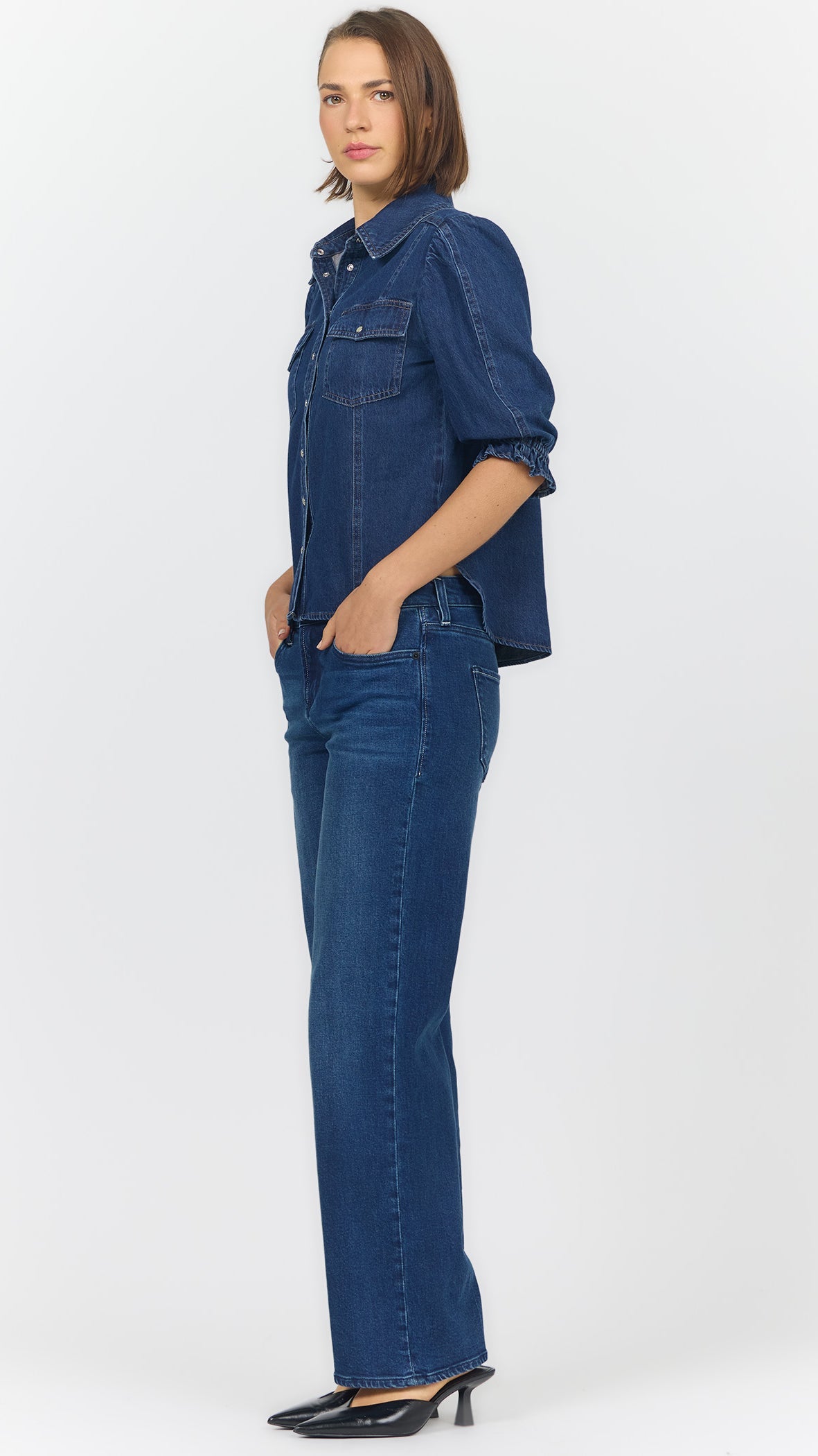 Full-length side view of Dear John Antonia dark cobalt denim blouse worn untucked with blue jeans and black slingback heels