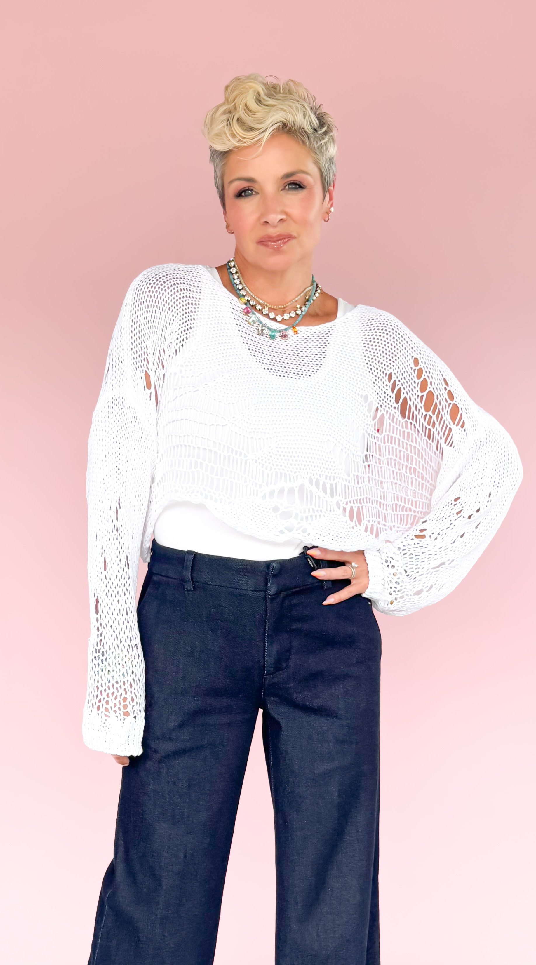 Woman wearing a white lace top and dark blue jeans against a pink background