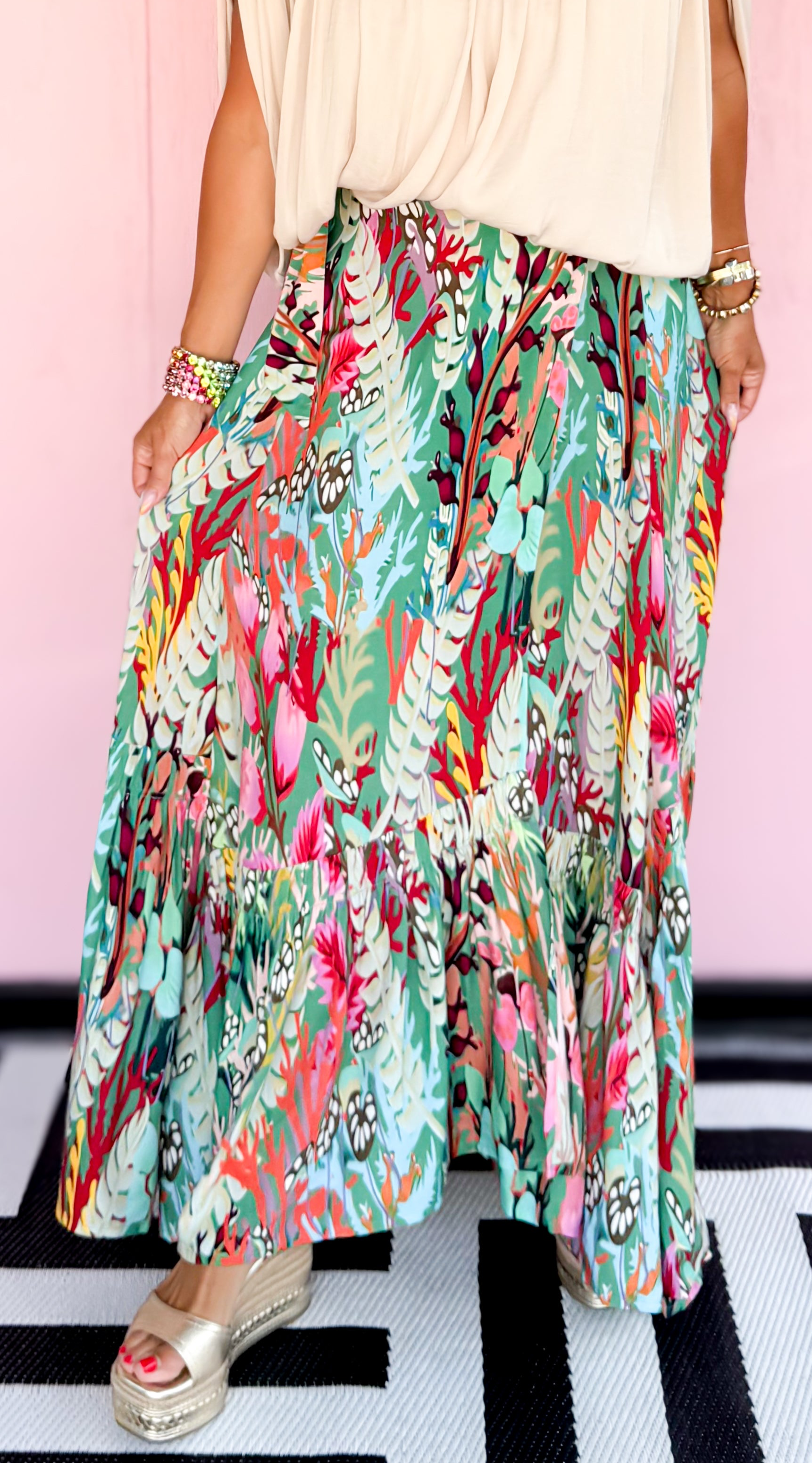 Woman wearing a floral skirt and beige top against a pink background