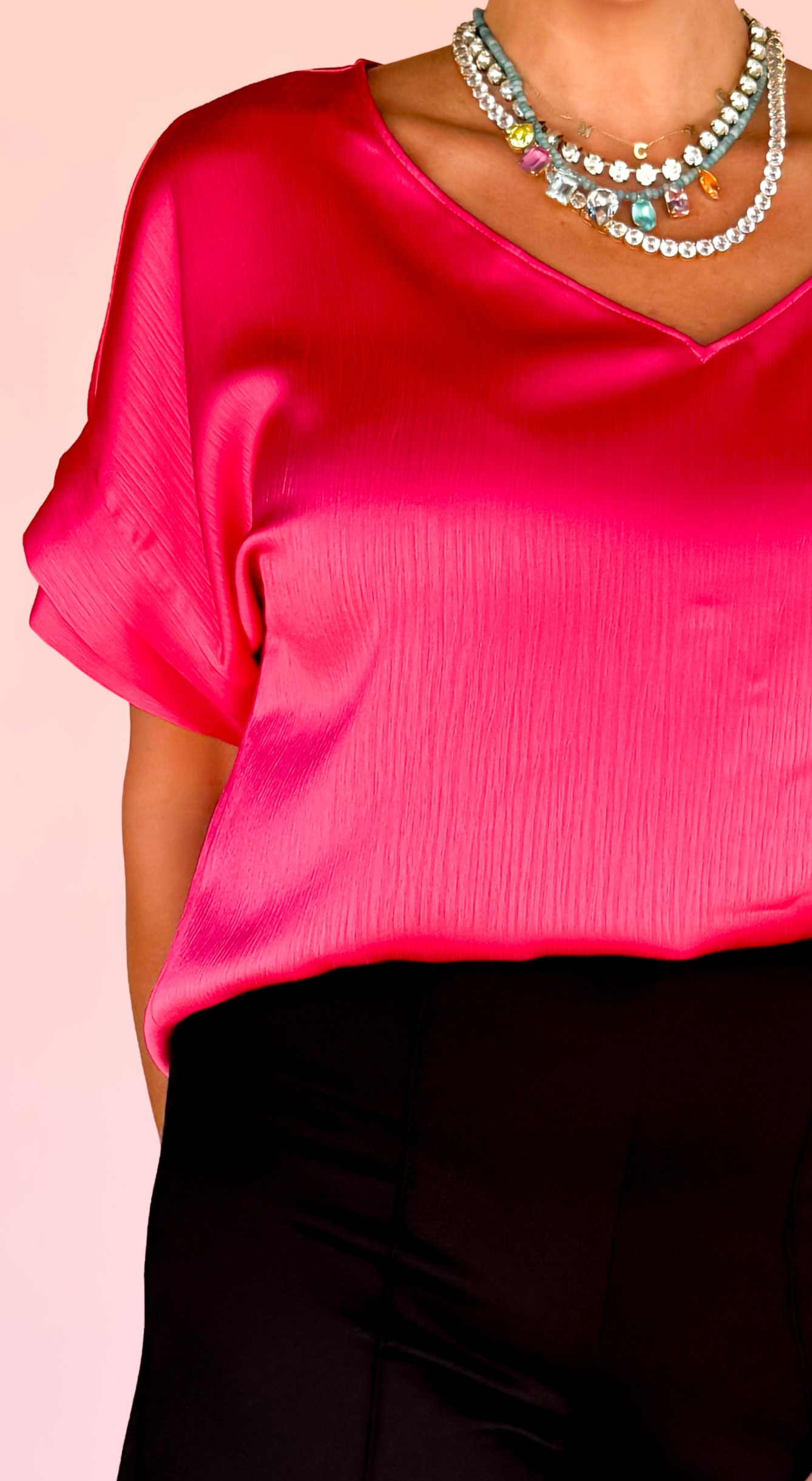 Woman wearing a bright pink top and black pants against a light pink background
