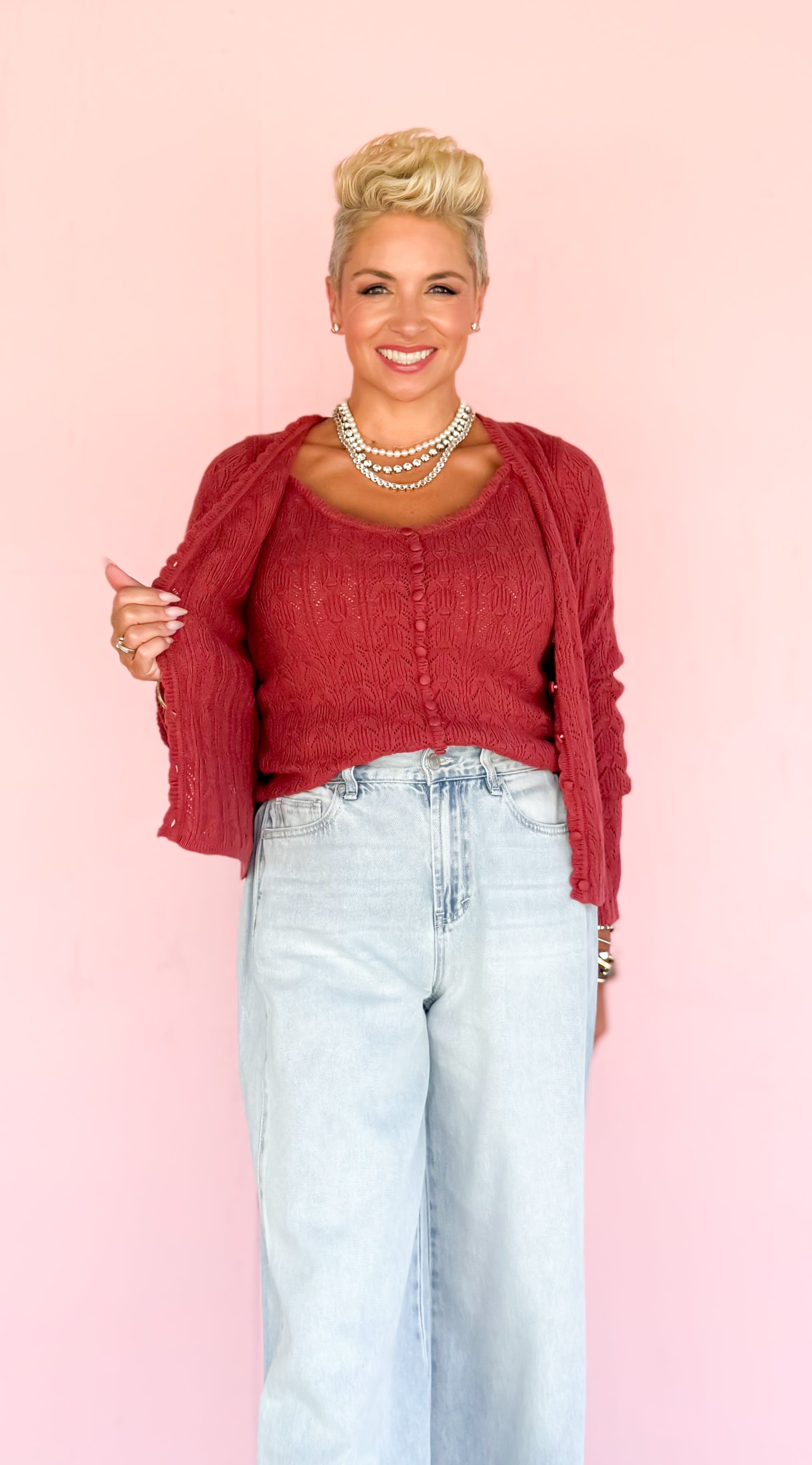 Person wearing a red cardigan and light blue jeans against a pink background