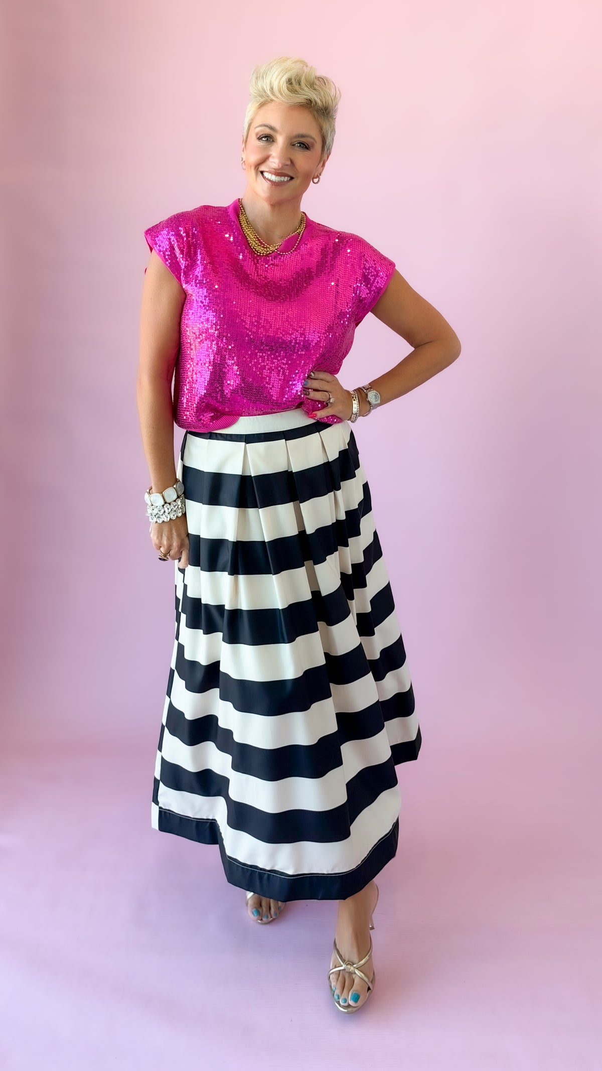 Hot pink Sierra sequin top worn with hand on hip and black and white striped skirt