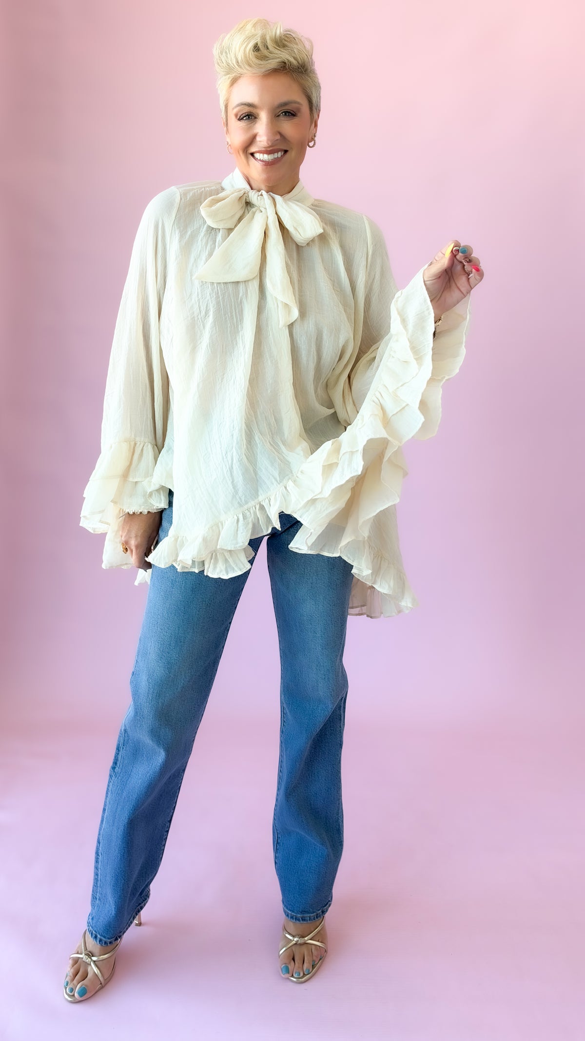 Model walking in cream oversized blouse with bow and ruffle trim