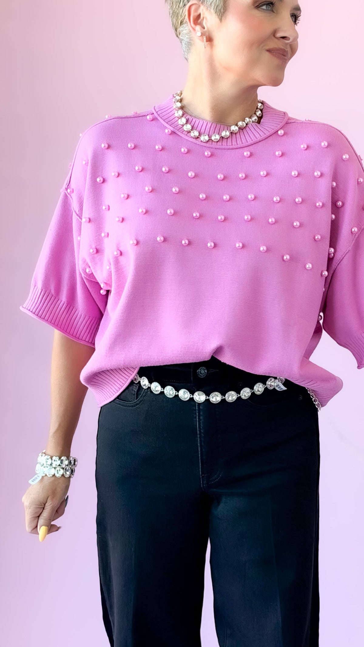 Pink pearl crewneck sweater worn with a pearl belt and black jeans