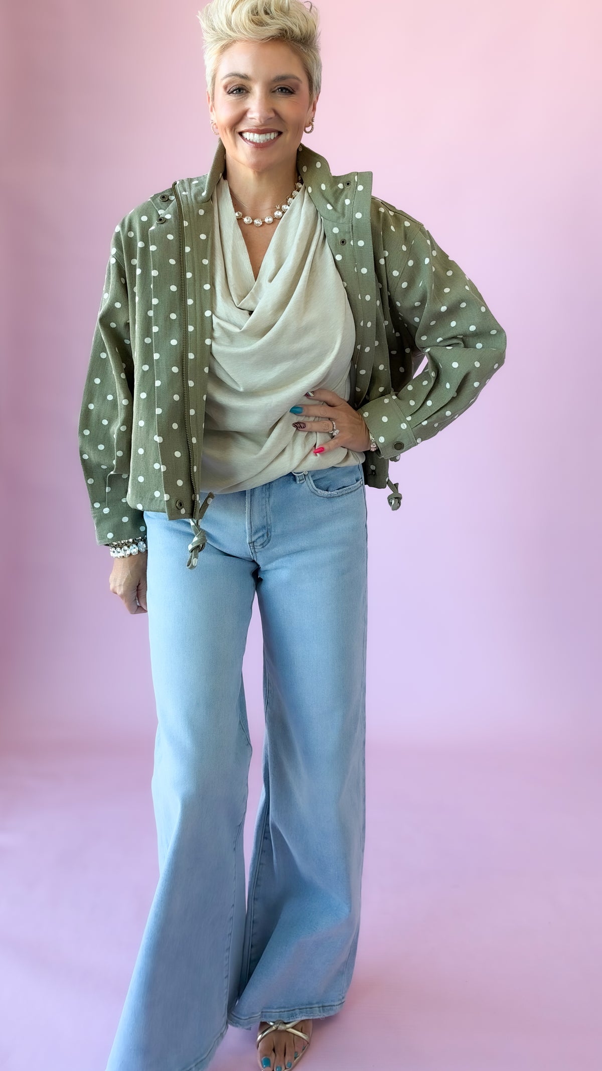 Full-length view of beige cowl neck top with olive polka dot jacket and wide-leg jeans