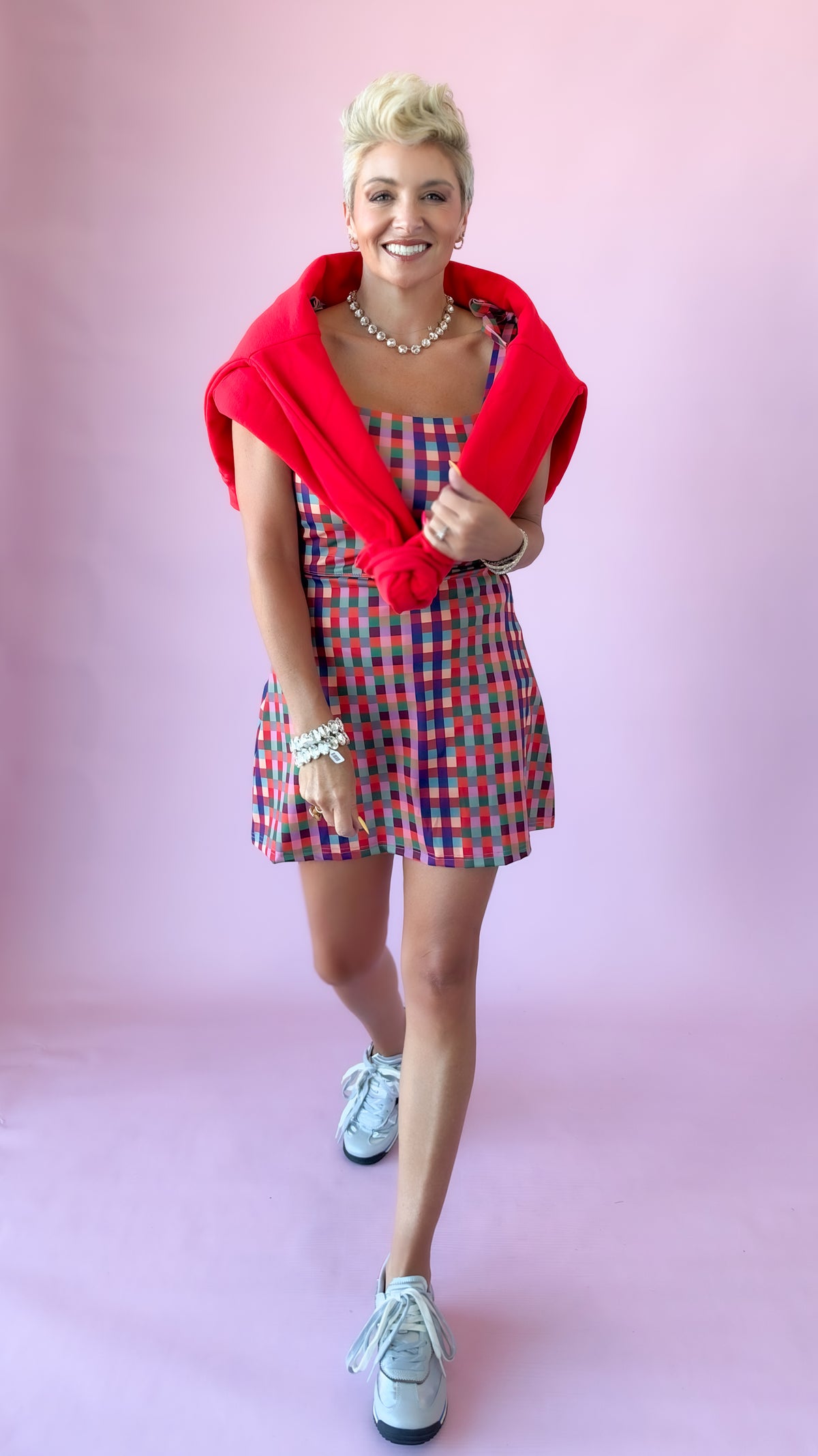 Gingham mini athletic dress styled with sneakers and a red sweater, mid-stride
