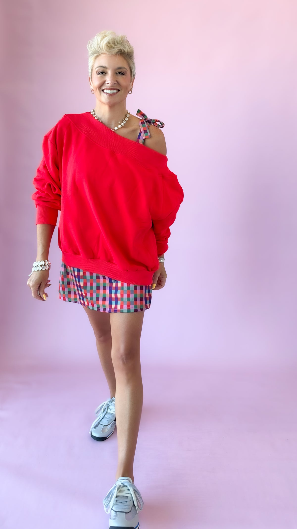 Model walking in red Harlow off-shoulder sweatshirt and plaid shorts