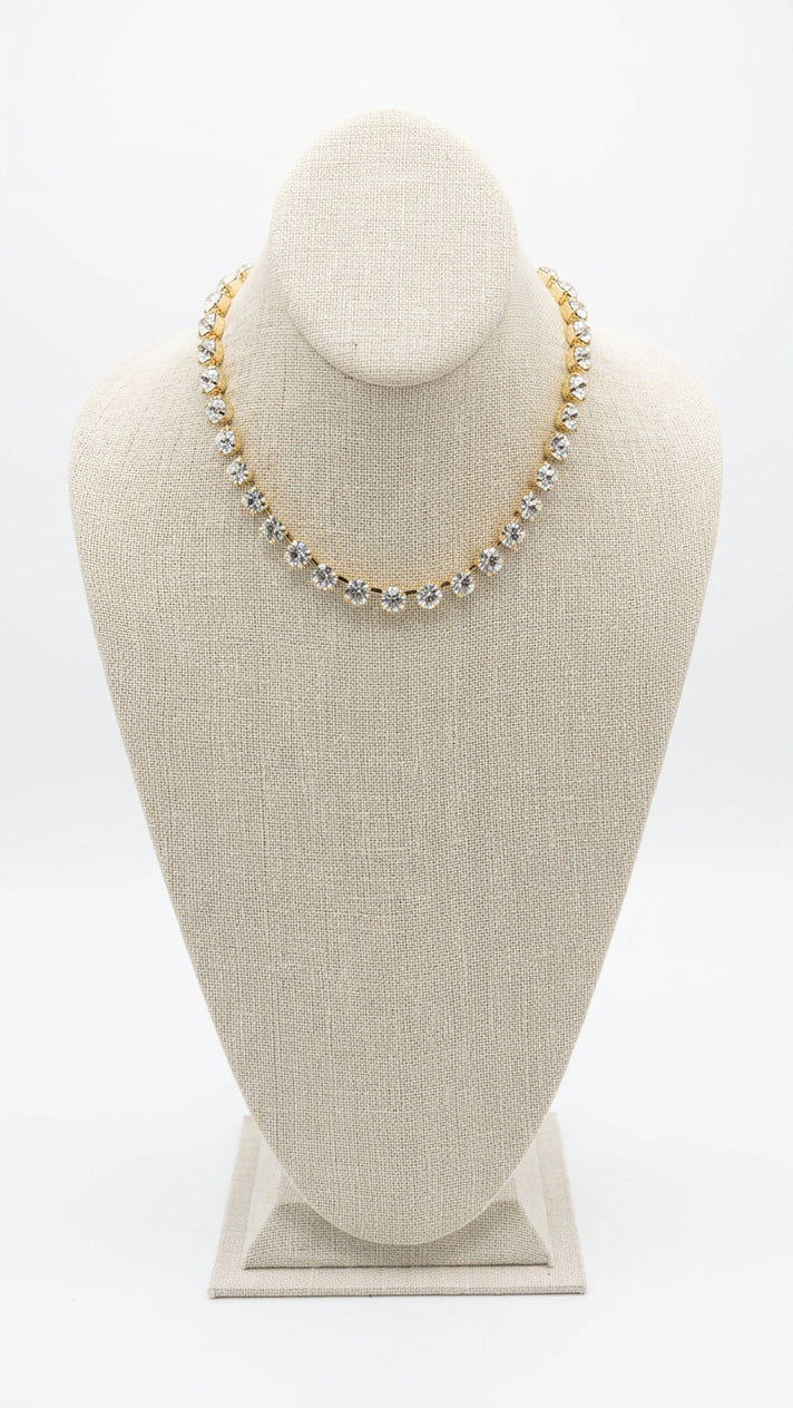 A gold chain necklace with clear rhinestones displayed on a beige fabric jewelry bust.