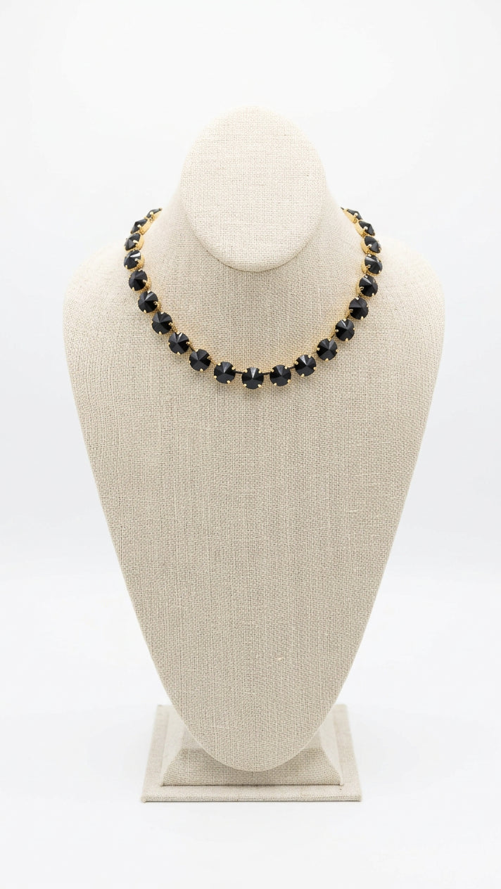 A black rhinestone necklace with gold-toned links displayed on a beige fabric jewelry bust.
