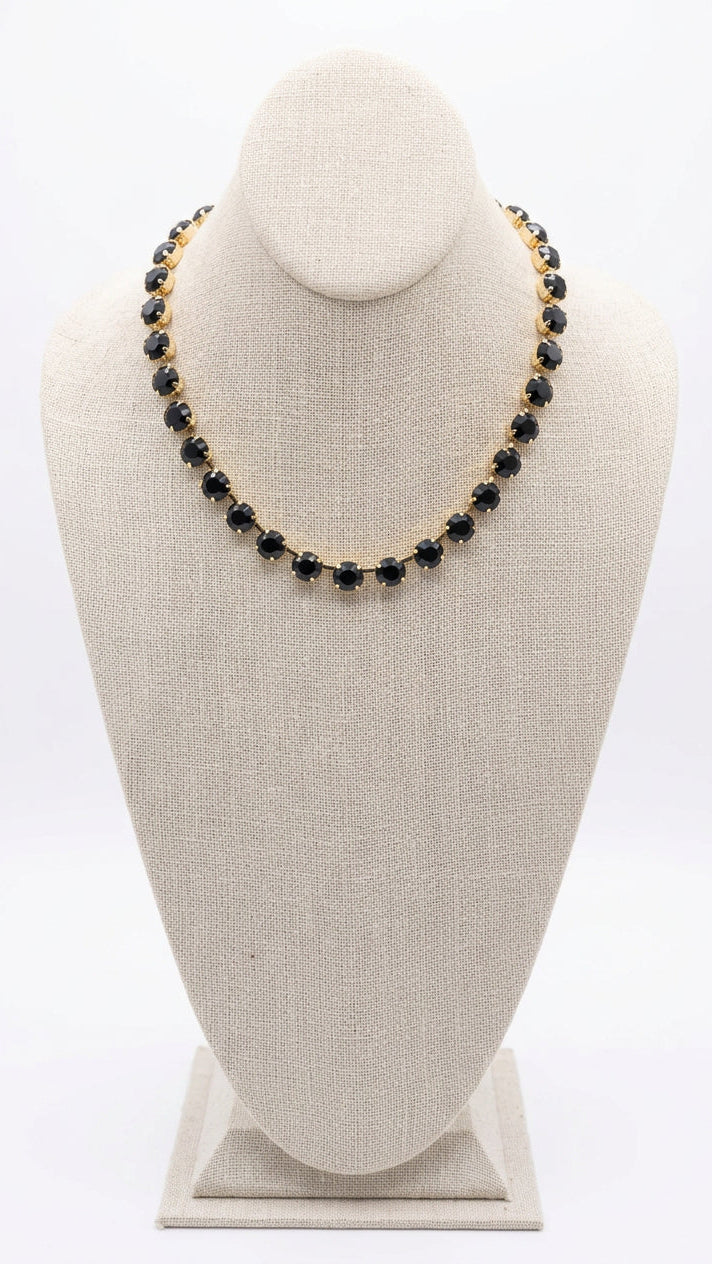 Black rhinestone necklace with gold metal on a beige bust.
