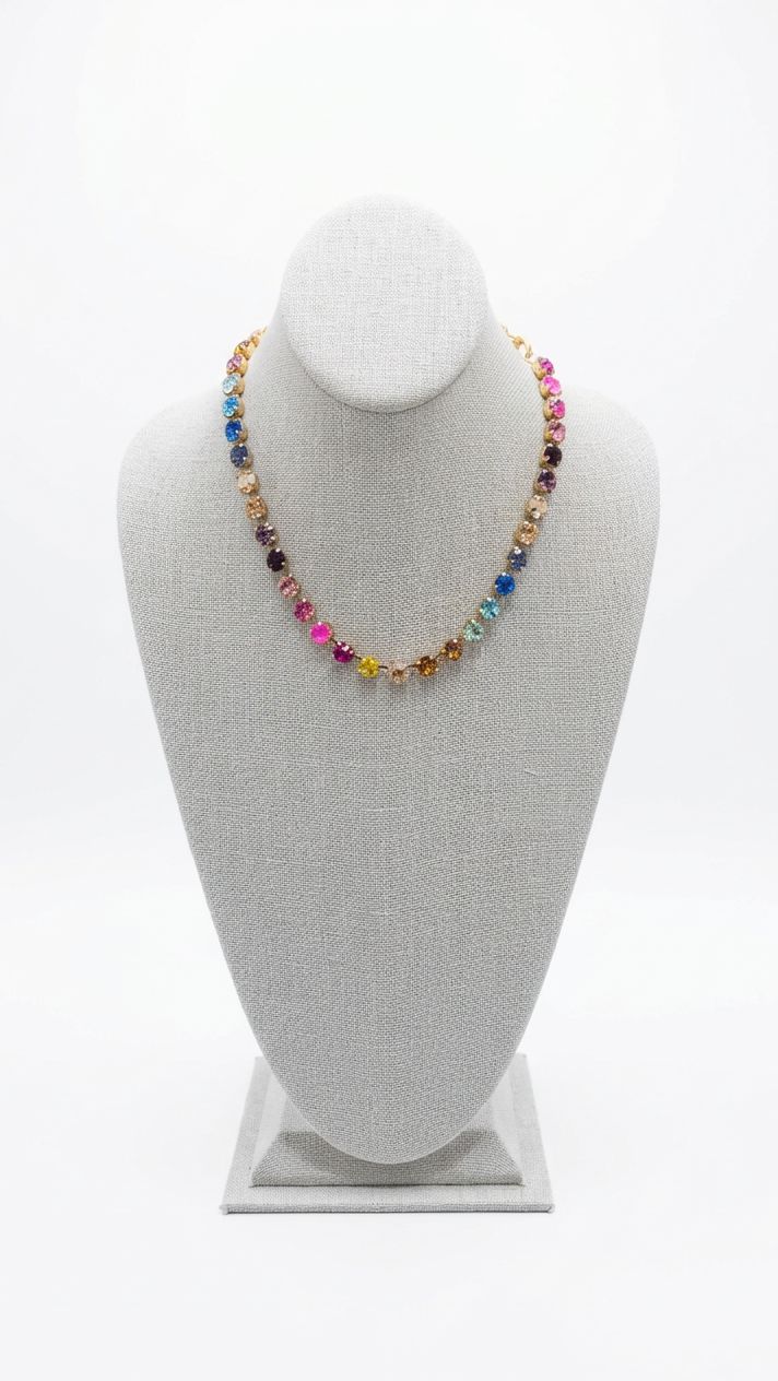 A colorful beaded necklace with gold-toned metal links displayed on a beige fabric jewelry bust. The necklace features multiple beads in pink, blue, yellow, orange, and purple tones.