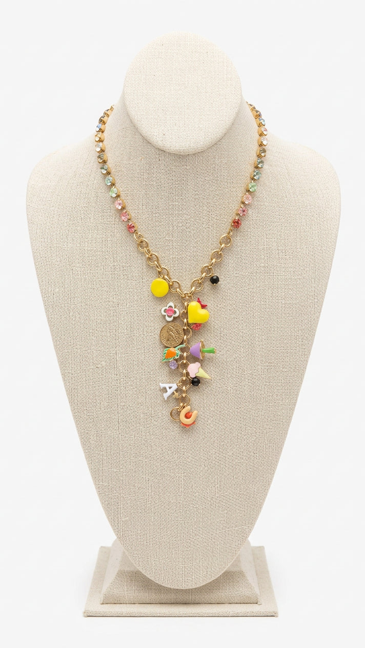 A gold-tone charm necklace displayed on a beige fabric jewelry bust. The necklace features a gold chain, a beaded section with pastel-colored beads, and a central cluster of colorful charms including yellow hearts, a rainbow star, and a small orange bird charm.