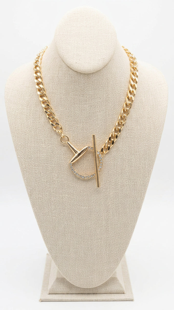 A gold-toned chunky chain necklace with a toggle clasp and small clear rhinestone accents, displayed on a beige fabric jewelry bust. 