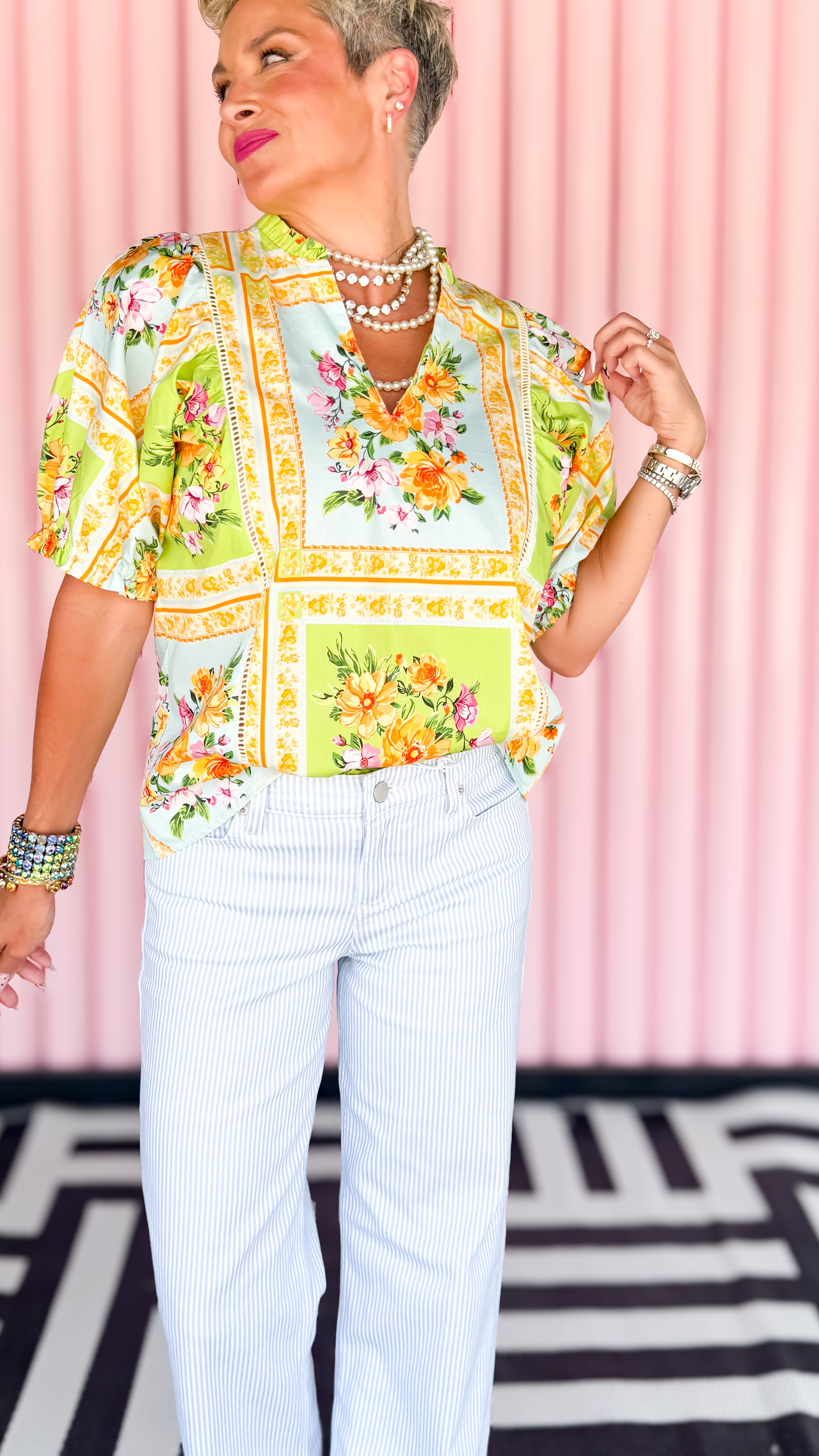 Person wearing a colorful floral blouse and white pants against a pink background