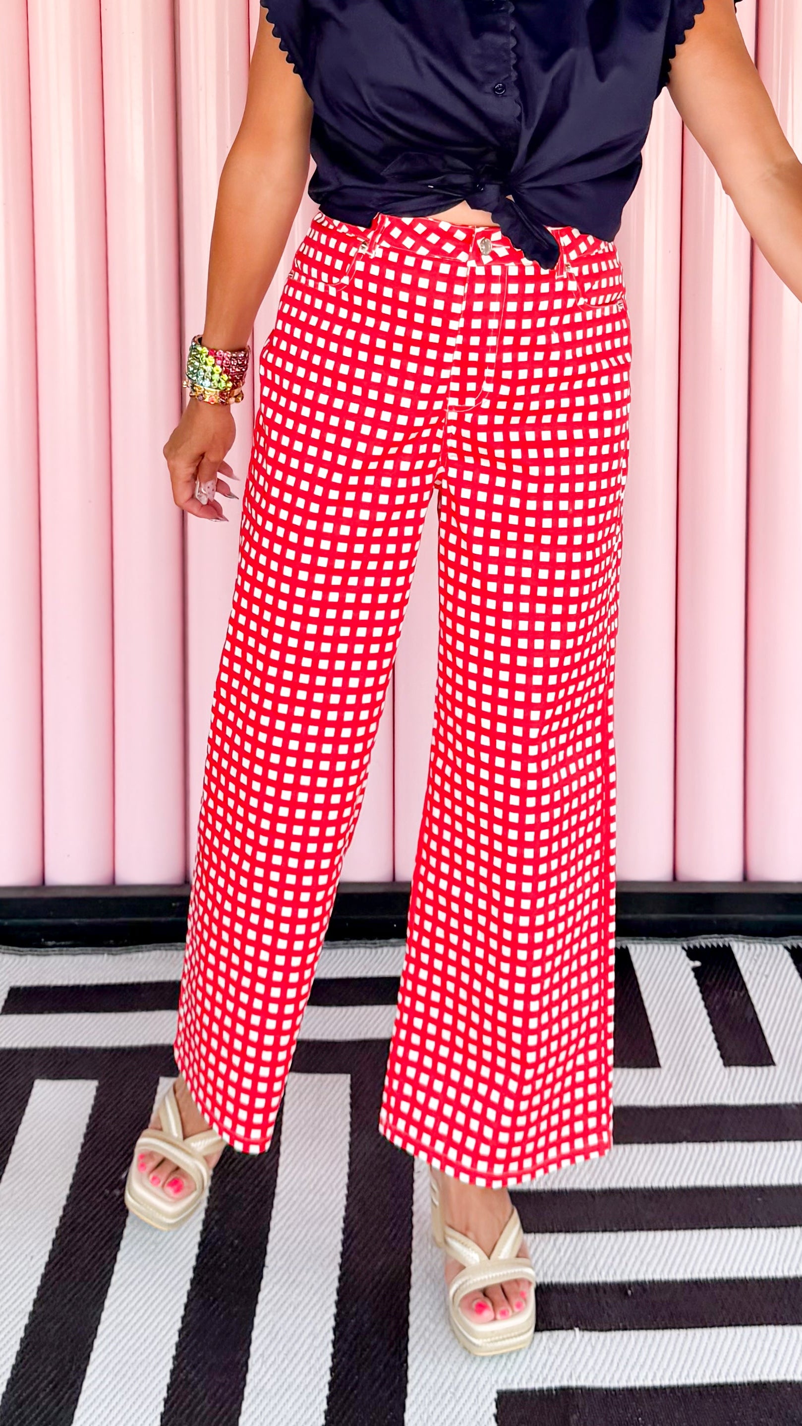 Woman wearing a navy top and red checkered pants against a pink striped wall.