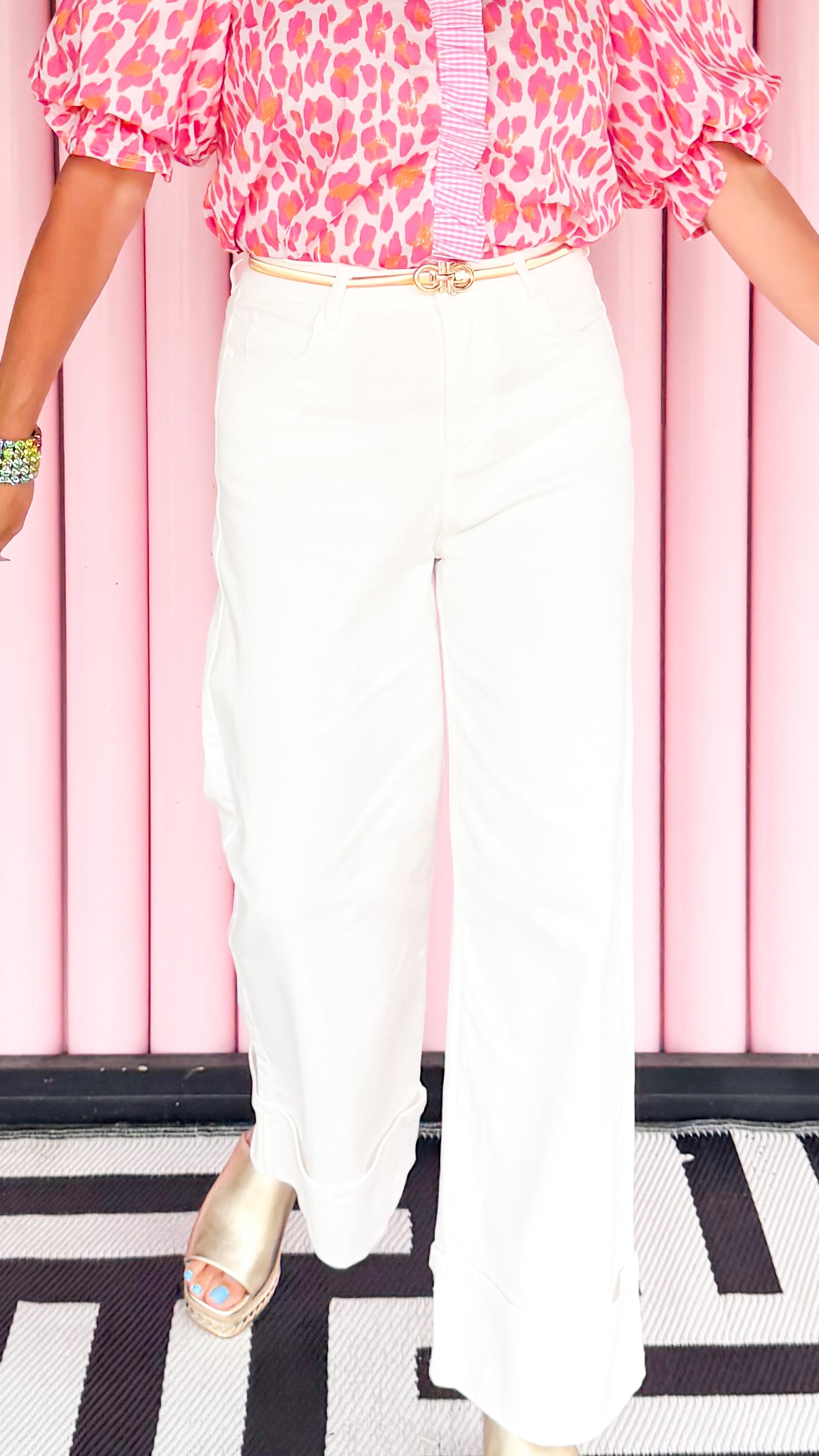 Woman wearing a pink leopard print blouse and white pants against a pink curtain background