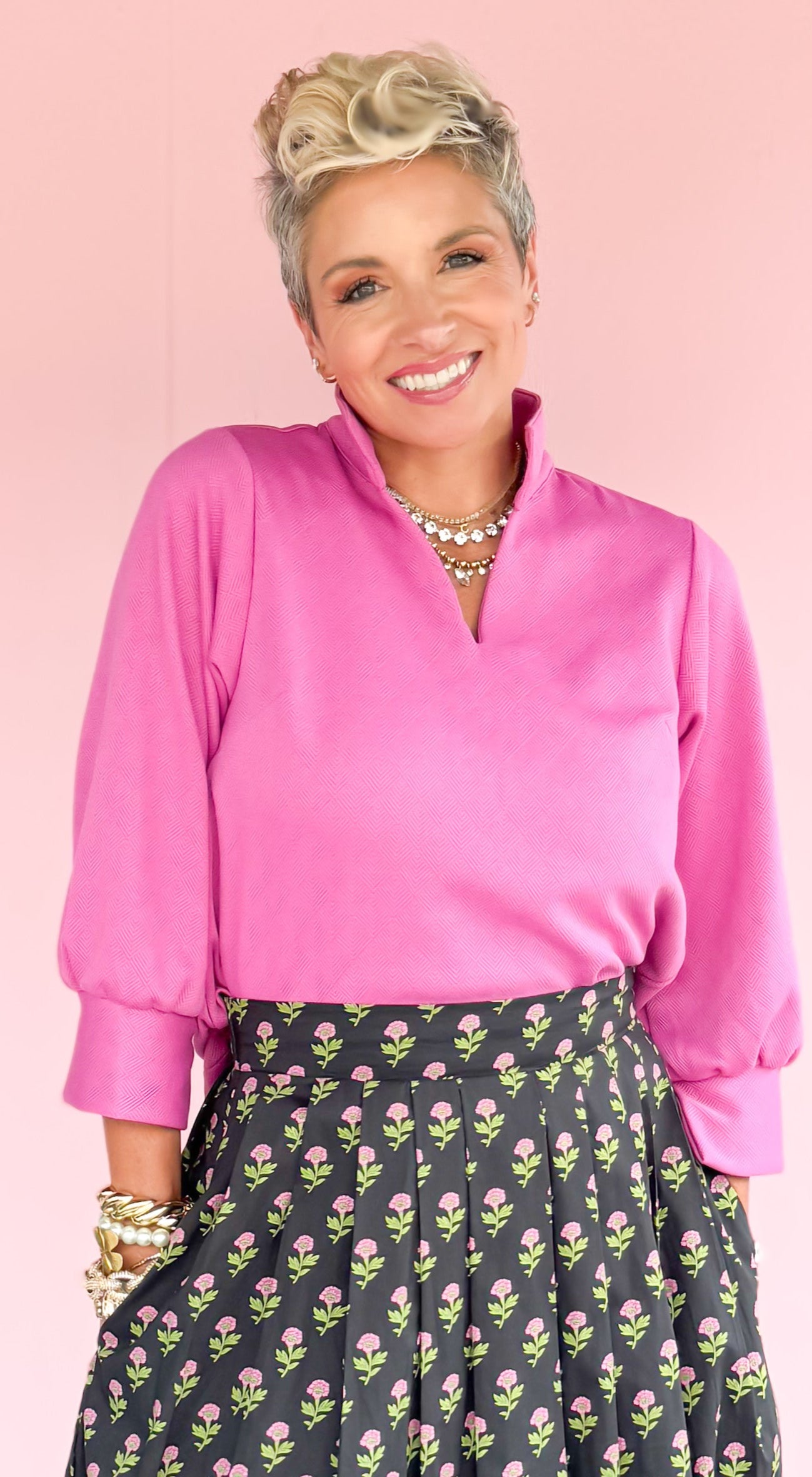 Woman wearing a pink blouse and floral skirt on a striped floor with a pink wall background