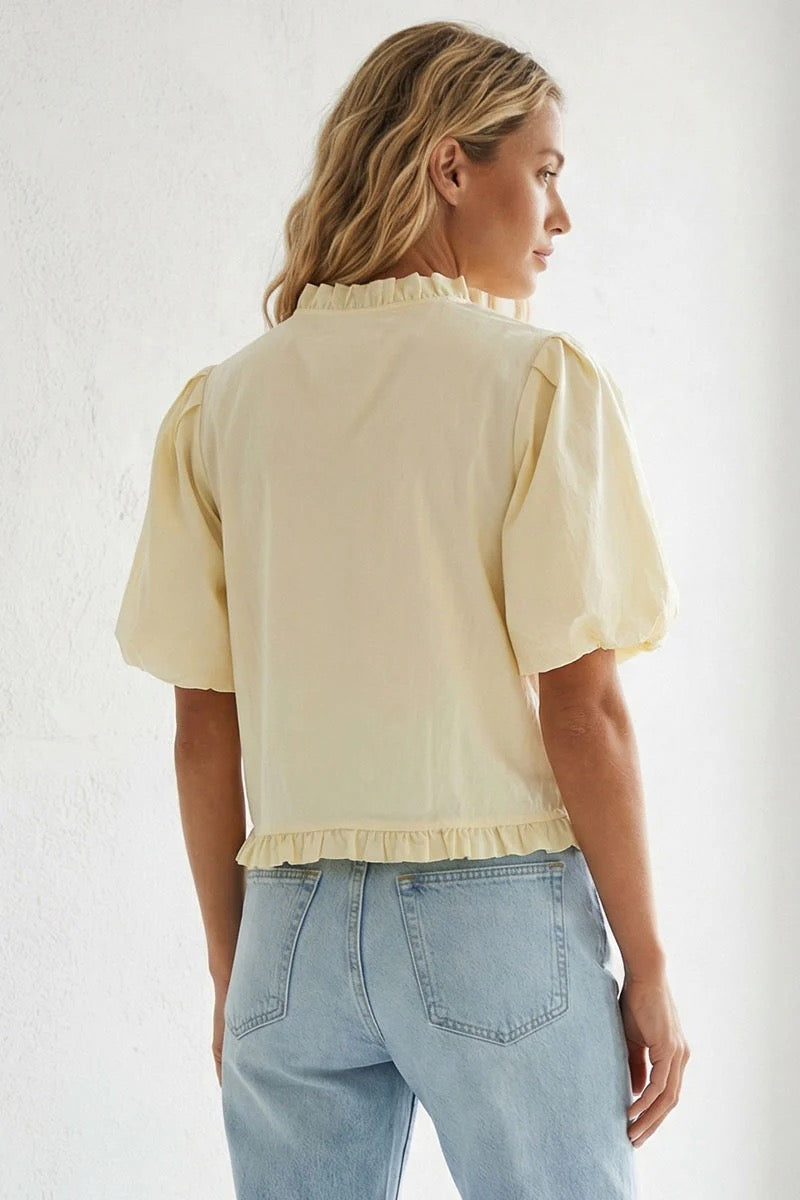Woman wearing a light yellow blouse with short sleeves and light blue jeans against a white background