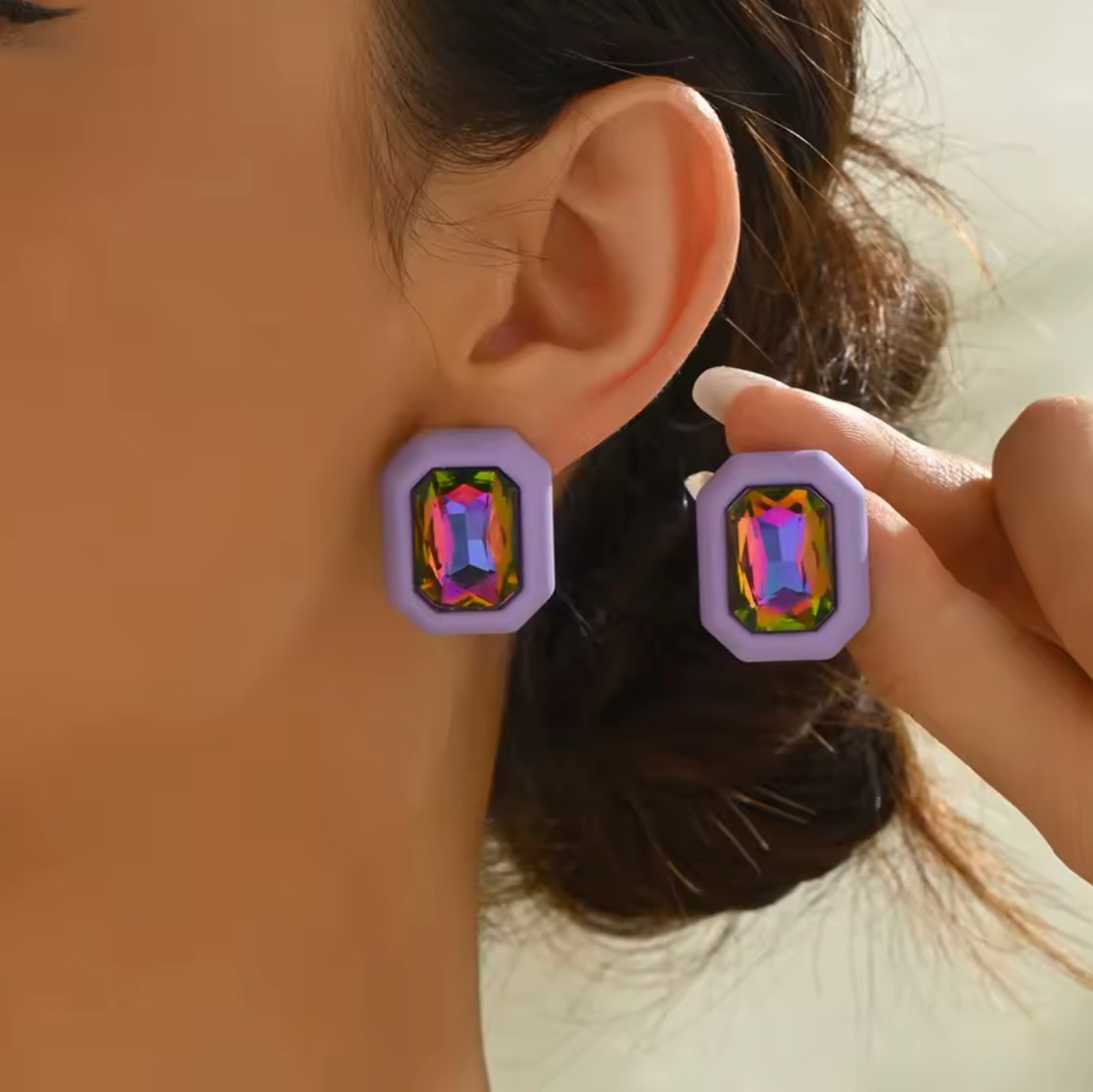 Close-up of a person wearing colorful square earrings with a blurred background