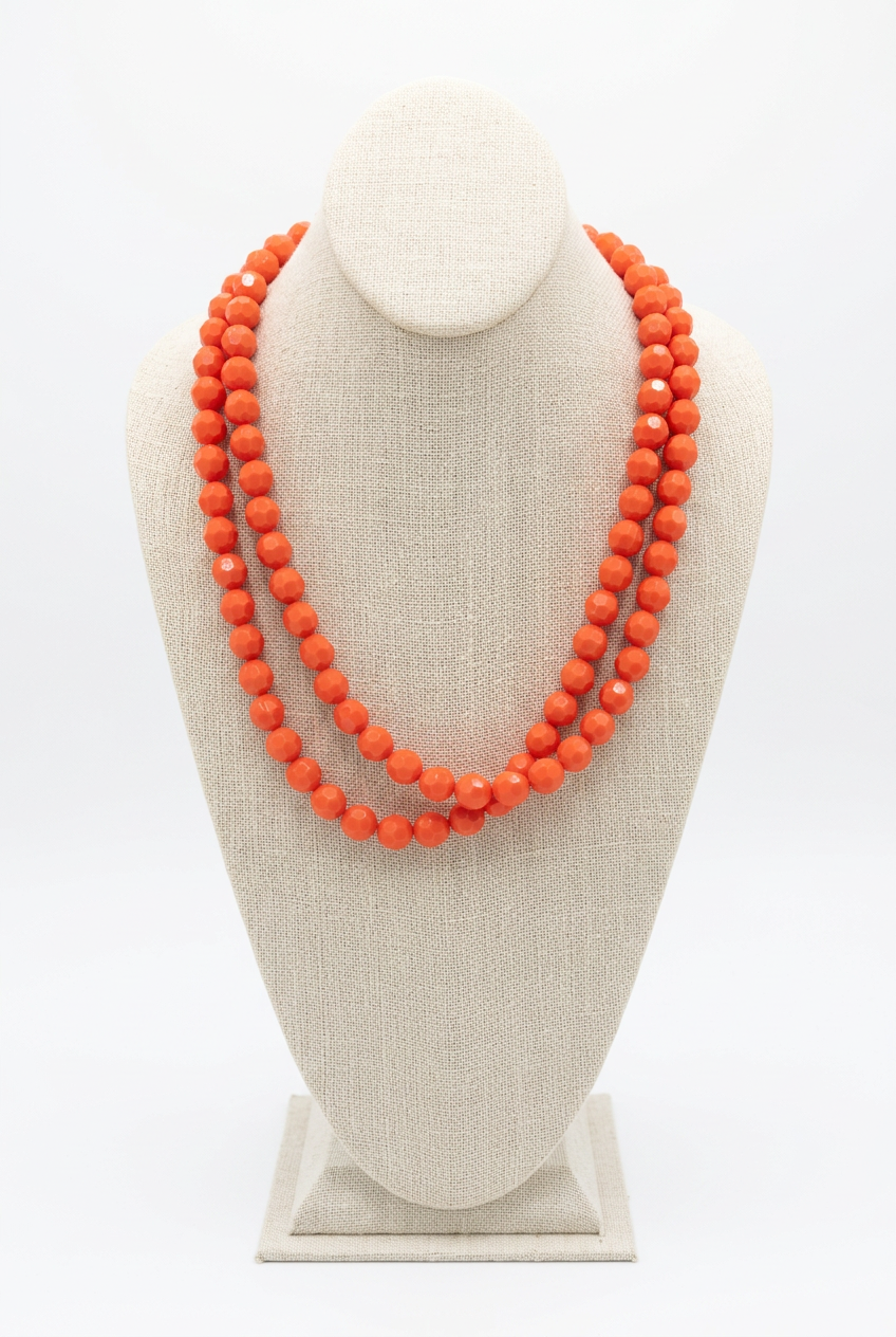 48-inch neon orange faceted bead necklace worn doubled in two layered strands on a beige linen jewelry bust