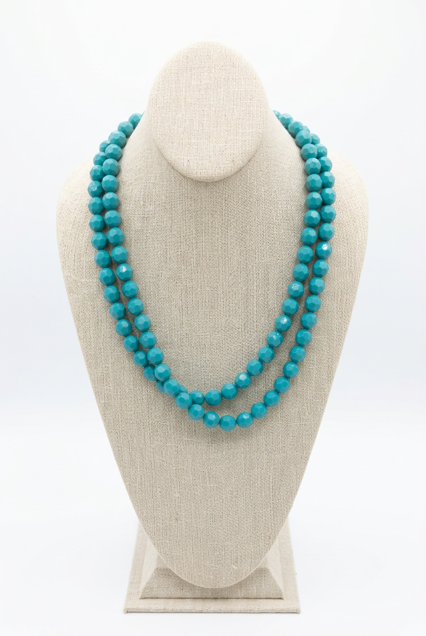 48-inch turquoise faceted bead necklace worn doubled in two layered strands on a beige linen jewelry bust