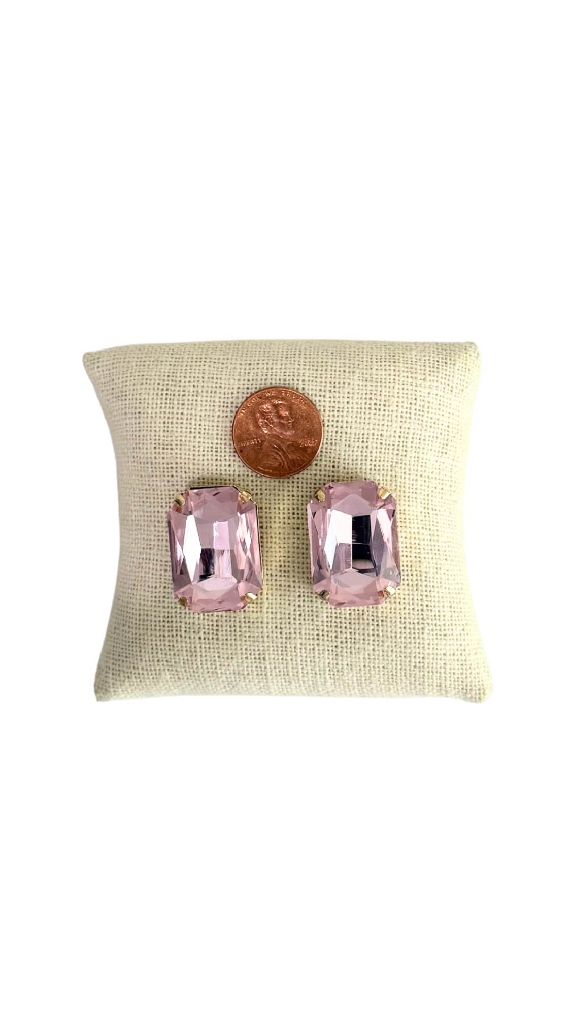 Pink gemstone earrings on a beige cushion with a white background
