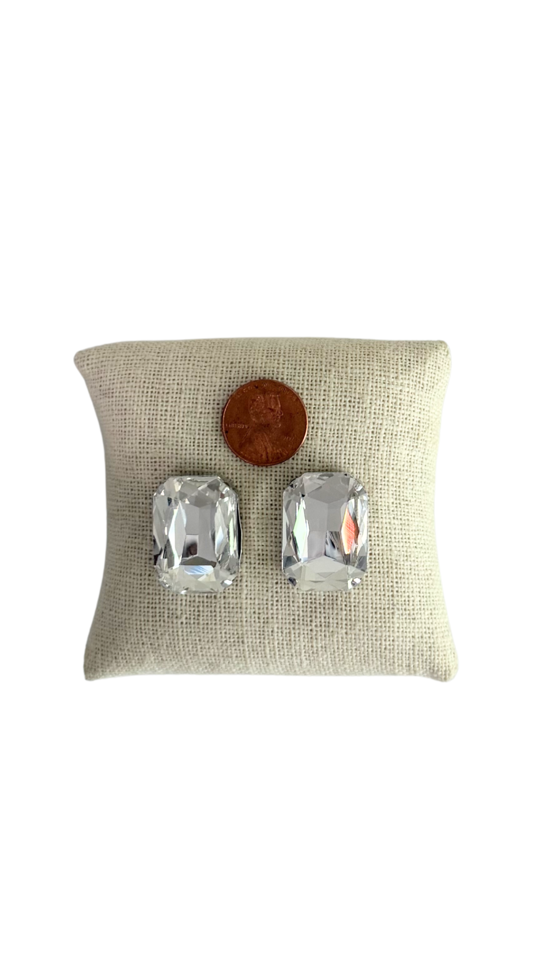 Pair of silver earrings on a beige pillow with a coin for scale on a white background