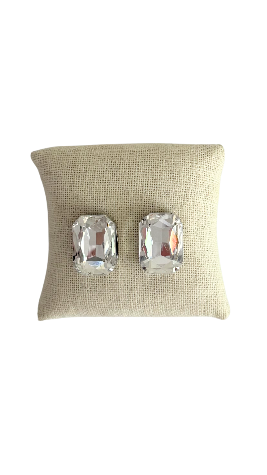 Pair of silver earrings on a beige cushion against a white background