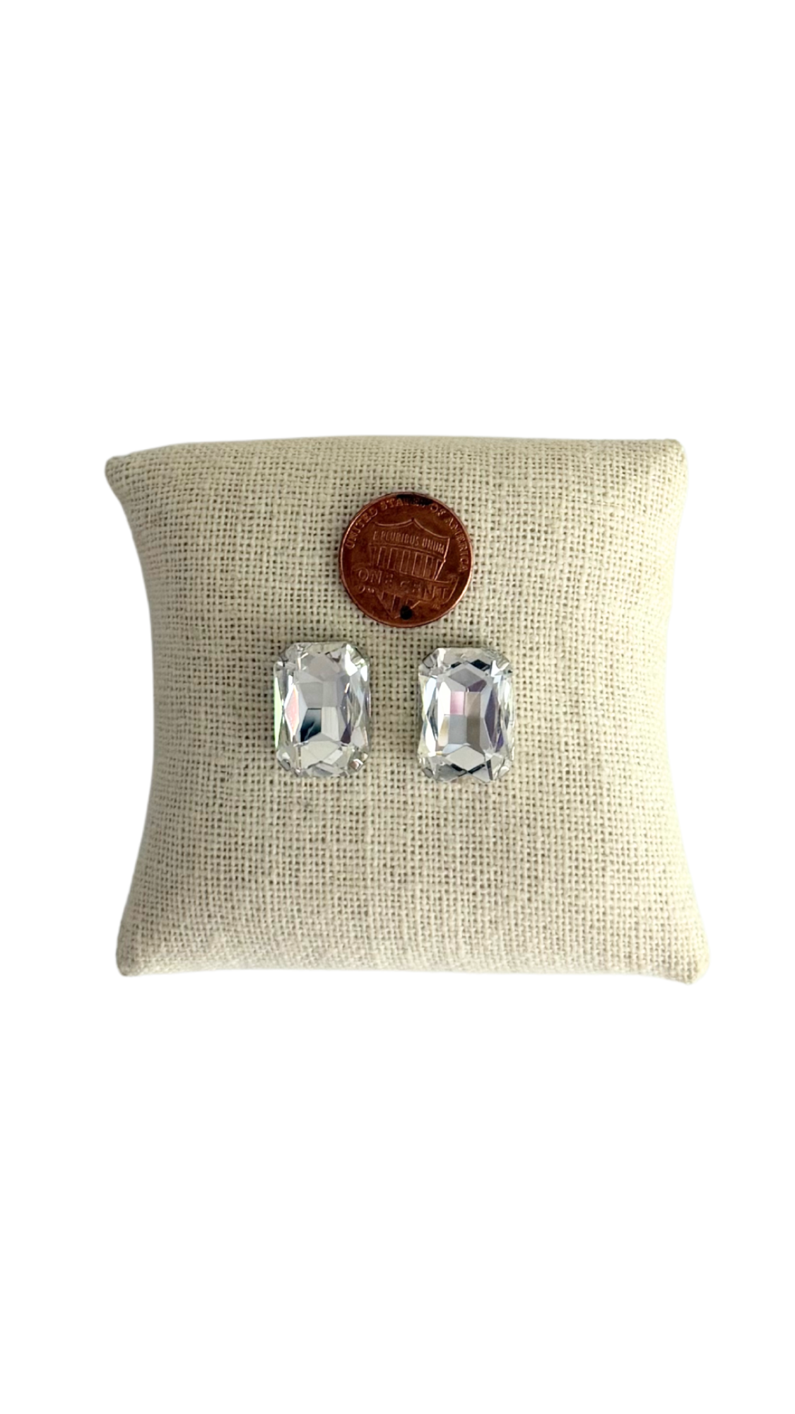 Pair of silver earrings on a beige pillow with a wooden button