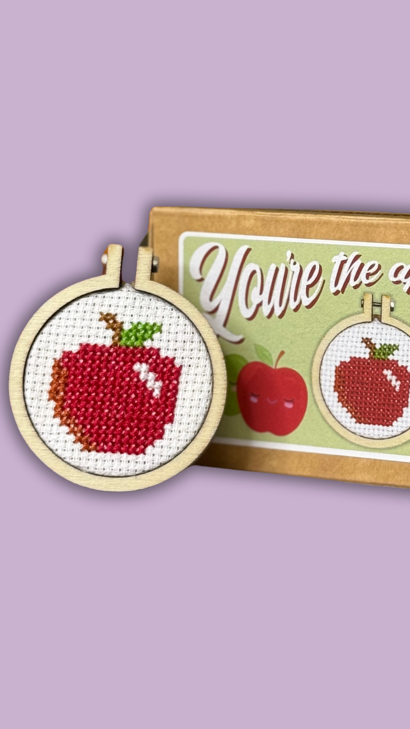 Cross-stitch mini kit with an apple design and packaging on a purple background