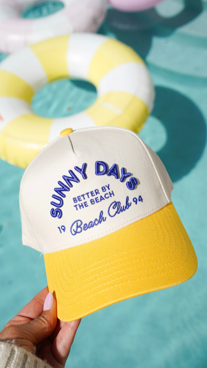Cap with 'Sunny Days Better by the Beach Club 94' text held in front of a pool float.