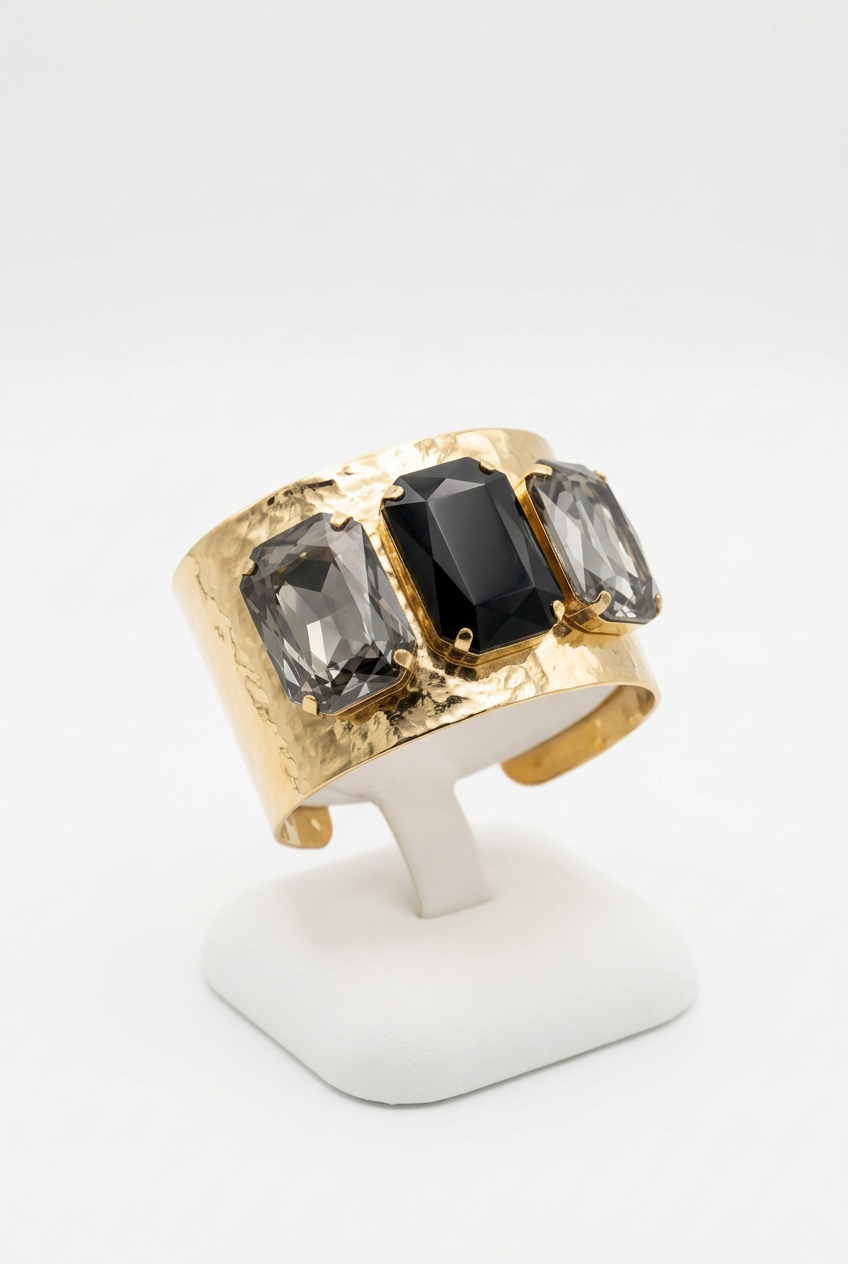 Gold-tone cuff bracelet with a dark rectangular center stone and smoky gray side stones on a white bracelet display.