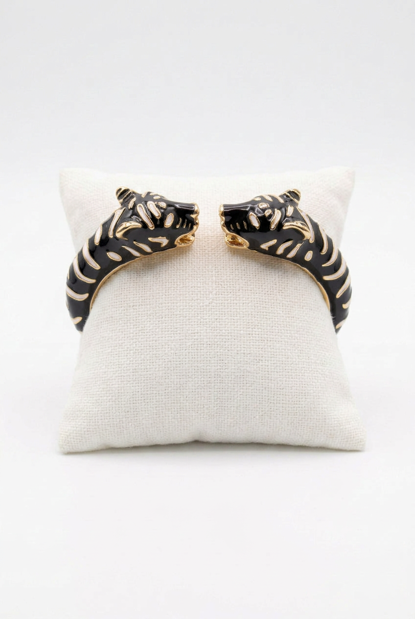 Black enamel double leopard-head cuff with gold-tone detailing on an ivory cushion against a white background.