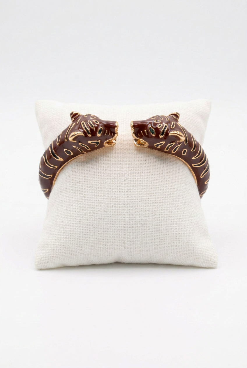 Brown enamel double leopard-head cuff with gold-tone detailing on an ivory cushion against a white background.