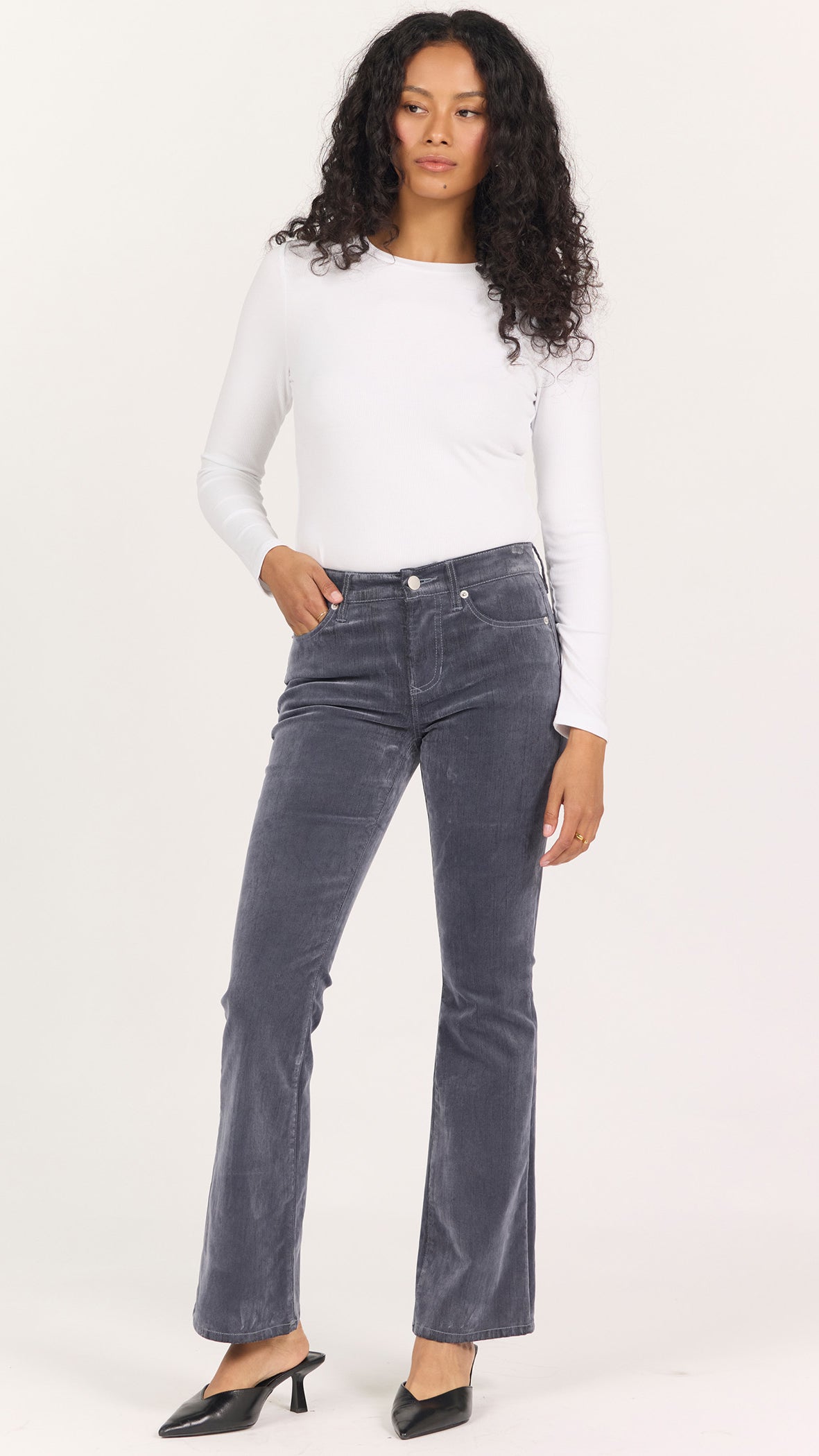 Full-length front view of Dear John Jaxtyn bootcut pants in smoke and mirrors gray velvet worn with a white long sleeve and black heels