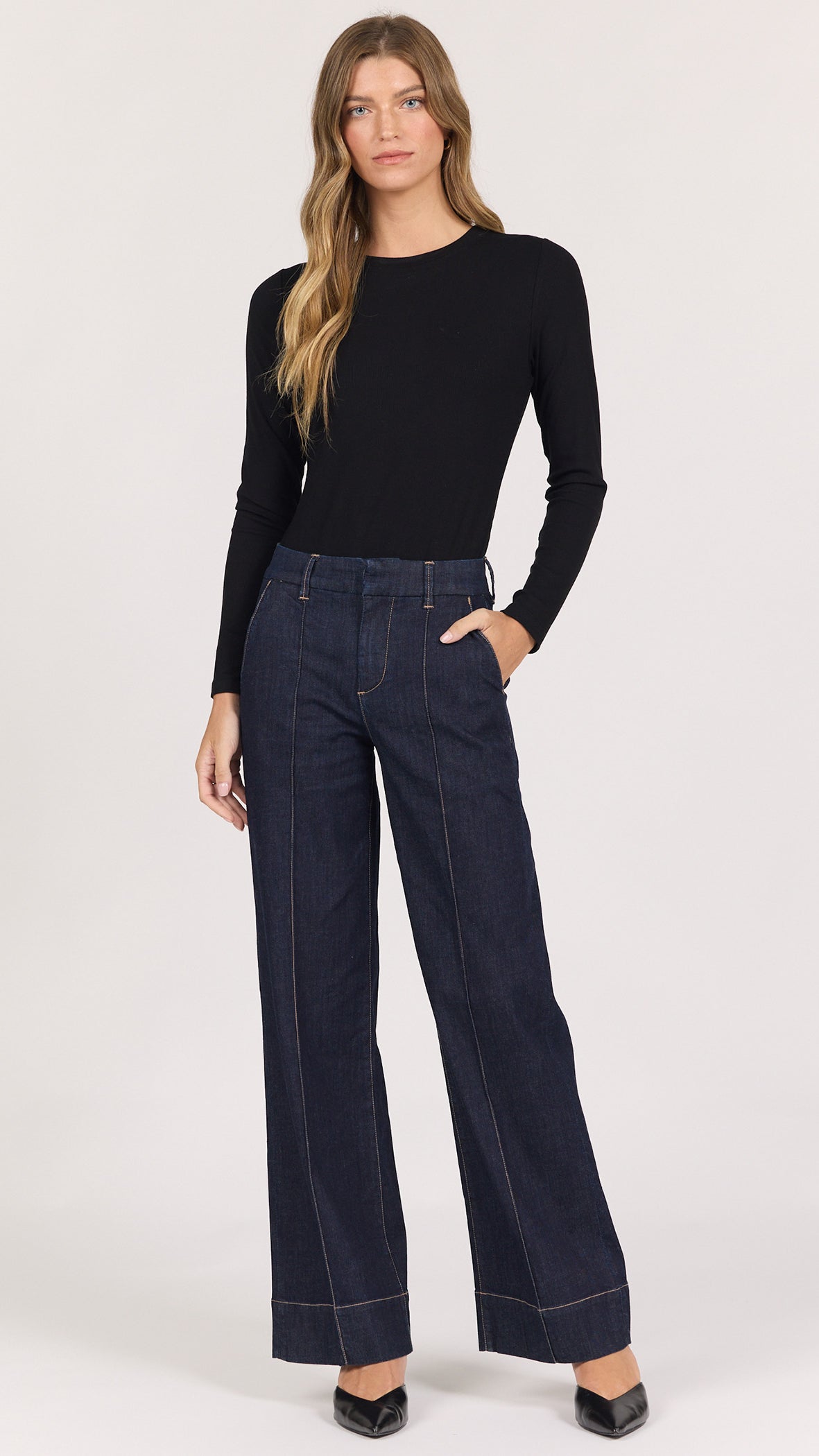 Full-length front view of Dear John Brandy wide leg denim trousers in equinox dark rinse worn with a black long sleeve and black pointed heels